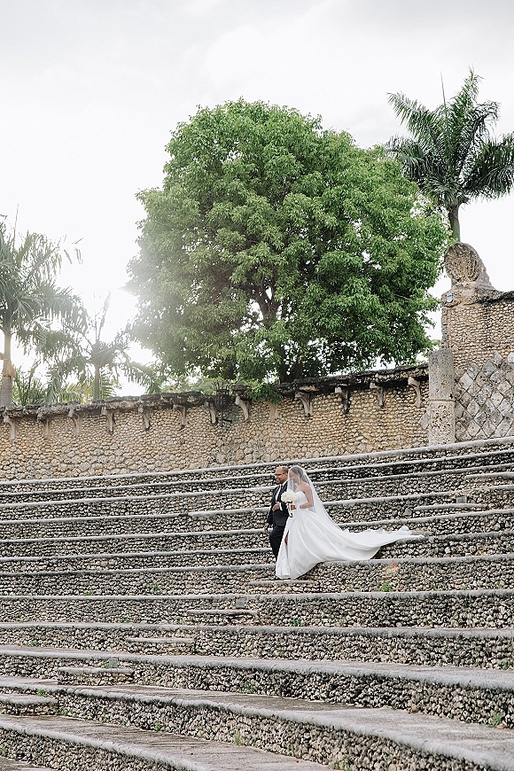 Wedding couple portrait of bride and groom walking down stone steps, her long veil and train flowing as she holds a white bouquet