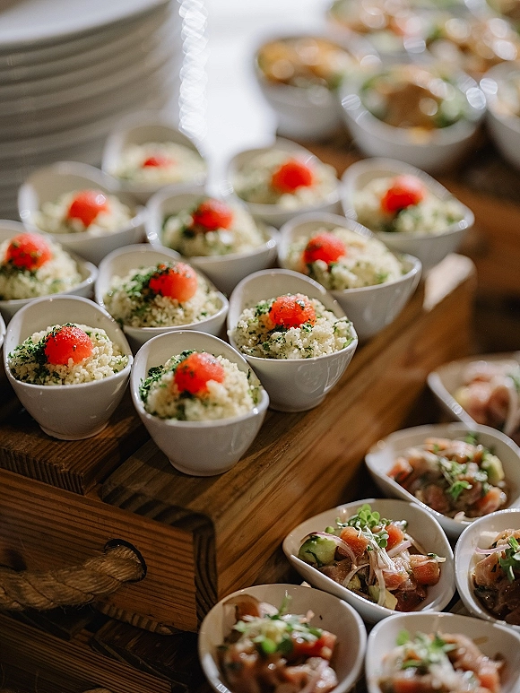 Wedding cocktail hour appetizers in white bowls and passed cups with microgreens, couscous salad and salmon tartare on wooden risers, buffet bokeh