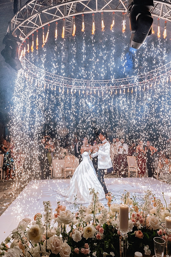 First dance with sparkler first dance bursts as bride in strapless gown and groom in white jacket twirl on a candlelit floor indoors