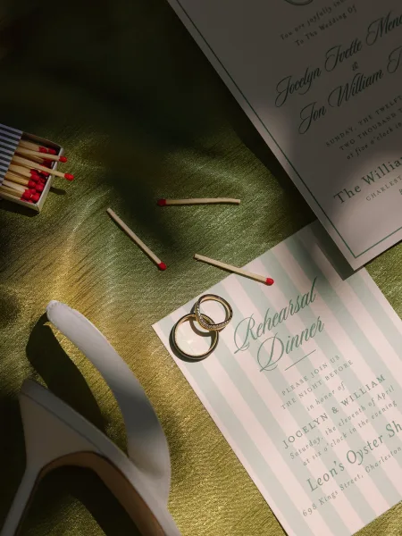 Rehearsal dinner invitation styled as a wedding stationery flatlay with wedding rings on green satin fabric.