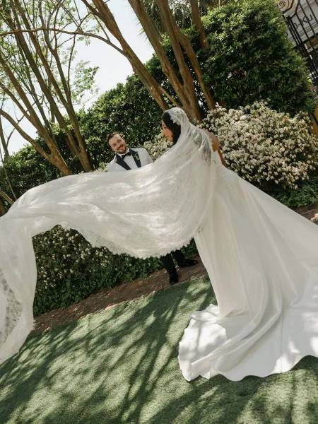 Couple portrait during their wedding first look, the bride's veil catching light by a wrought iron gate and flowering garden.