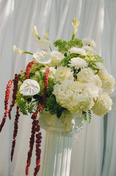 Ceremony floral arrangement styled as altar flowers with hydrangeas, set against a white drapery backdrop.