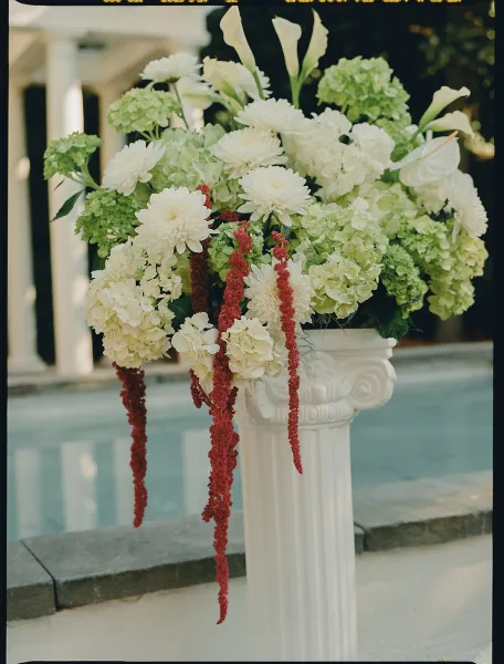 Ceremony floral arrangement of white and green wedding flowers with lush hydrangeas set poolside beside a stone ledge and garden trees.