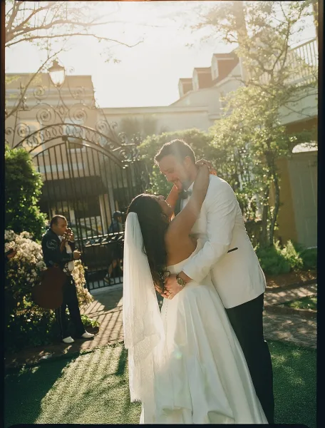 Wedding first dance as an outdoor wedding portrait, the bride’s veil trailing as they sway in a garden courtyard by a wrought iron gate.