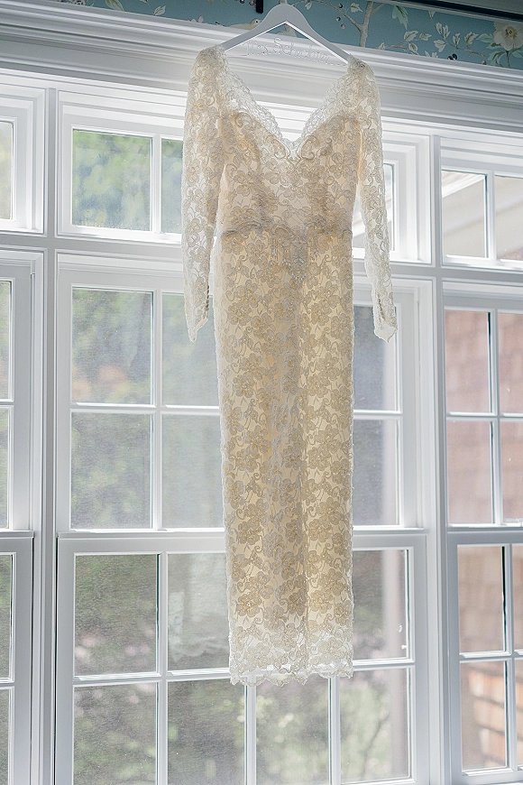 Wedding dress, lace wedding dress on a hanger with long sleeves and V-neckline, hanging in a window with soft natural light