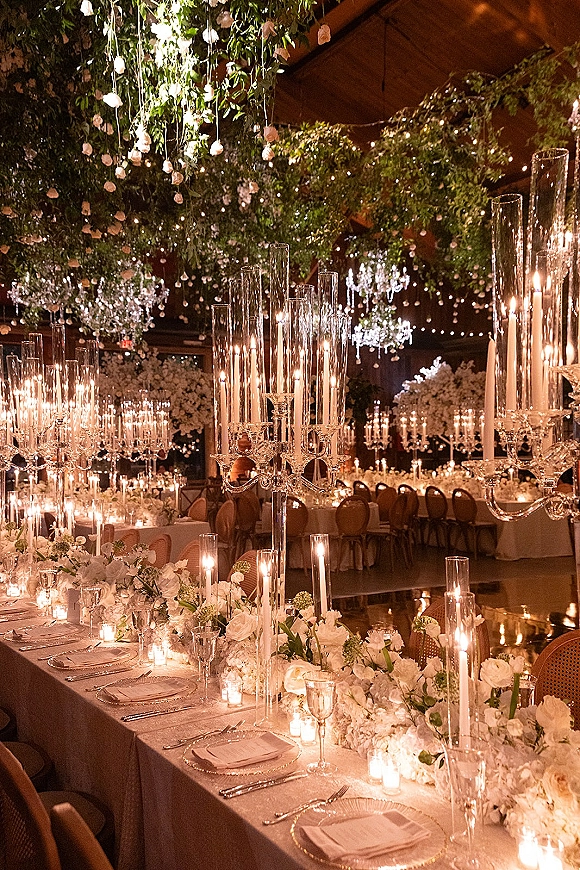 Reception tablescape with candlelit wedding reception glow, tall glass cylinder candles and white floral garland on long tables under chandeliers