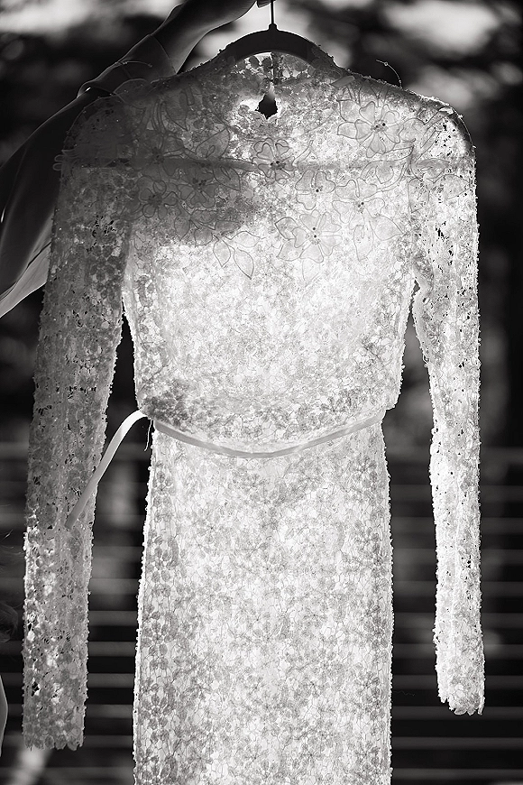 Wedding dress, lace wedding dress with long sleeves and floral appliqué, hanging on a hanger on outdoor steps with tree bokeh behind