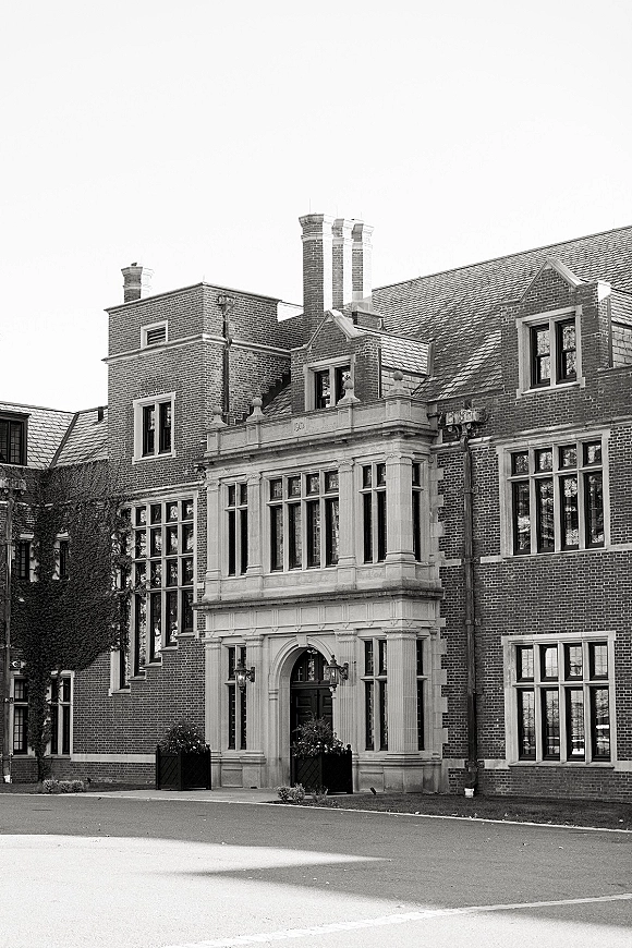 Wedding venue exterior of a brick manor wedding venue with ivy-framed arched doorway, lantern sconces, planters, and driveway approach