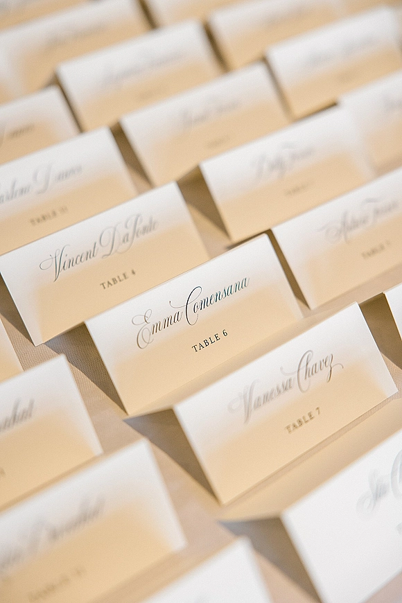 Wedding place cards with calligraphy place cards in black ink, folded tent escort cards arranged on a linen tablecloth at reception