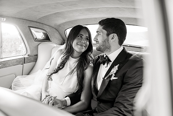 Couple portrait in a wedding car photo, bride and groom in car holding hands in vintage leather backseat with veil and tuxedo