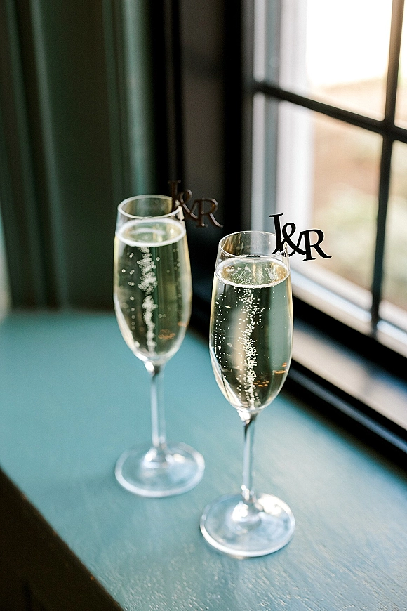 Champagne toast with champagne flutes of sparkling wine and monogram drink charms on a tabletop by bright window light