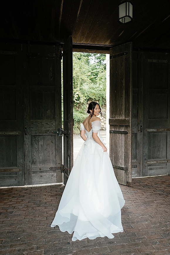 Bridal portrait of a bride in an off the shoulder wedding dress, looking over her shoulder by rustic barn doors under lantern light
