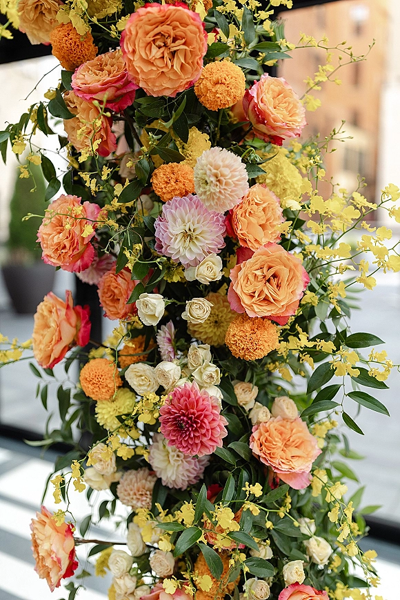 Wedding floral installation ceremony floral pillar with roses, dahlias, and yellow orchids cascading against a city street backdrop