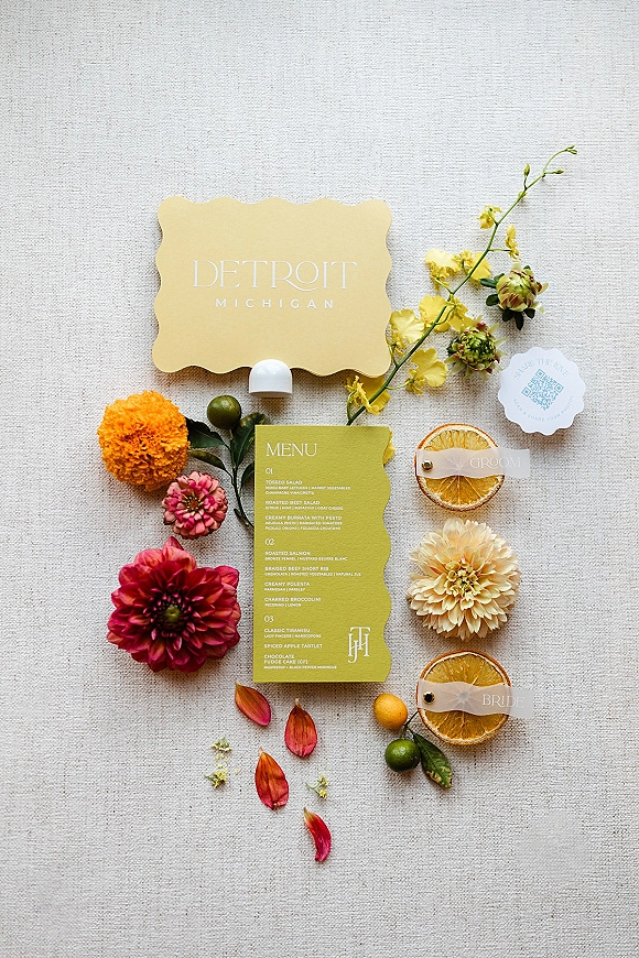 Invitation suite wedding flat lay with scalloped menu and place cards, cocktail tags, florals, and dried citrus slices on linen backdrop