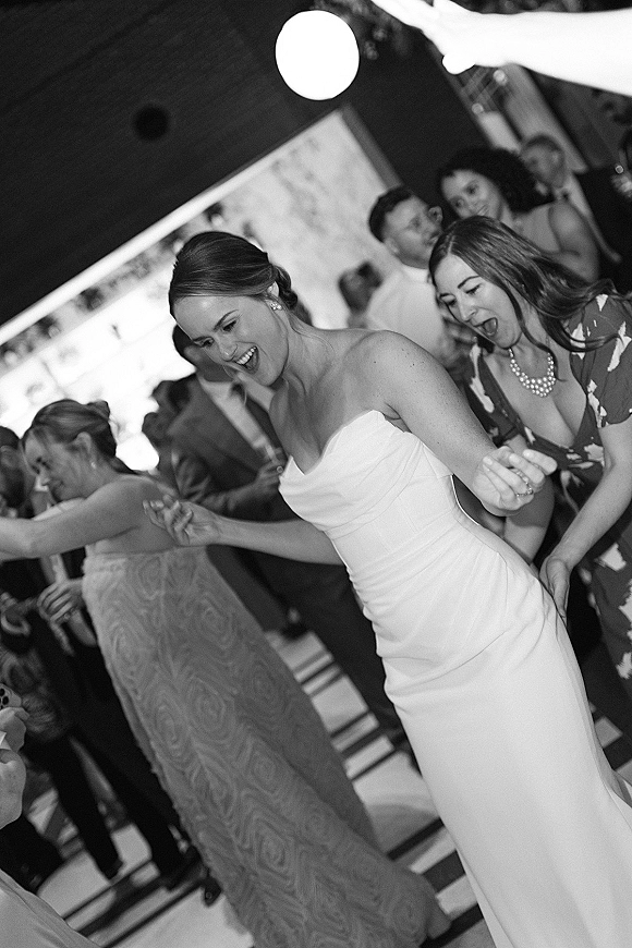 Wedding dance floor packed with guests as the bride dancing reception in a strapless dress and pearl necklace under a round ceiling light