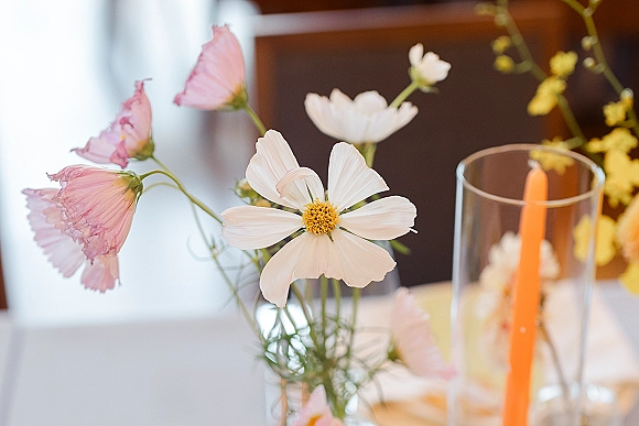 Wedding table centerpiece with wildflower wedding centerpiece in a glass vase beside taper candle and hurricane on white tablecloth, wooden wall backdrop