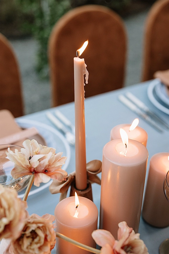 Reception tablescape with wedding candle centerpiece, taper and pillar candles among blush blooms, set on a soft blue tablecloth with chairs and greenery