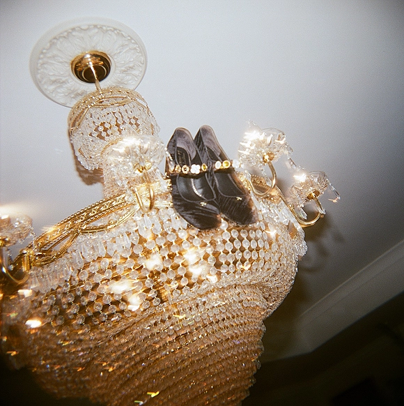 Bridal shoes, wedding shoes flatlay of black ankle-strap heels perched on a gold-framed crystal chandelier against the ceiling backdrop