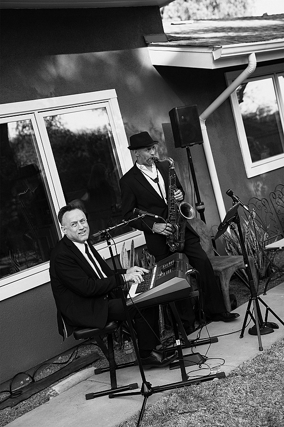 Wedding live music duo playing saxophone and keyboard at patio cocktail hour, with microphones and speakers outside a house with plants