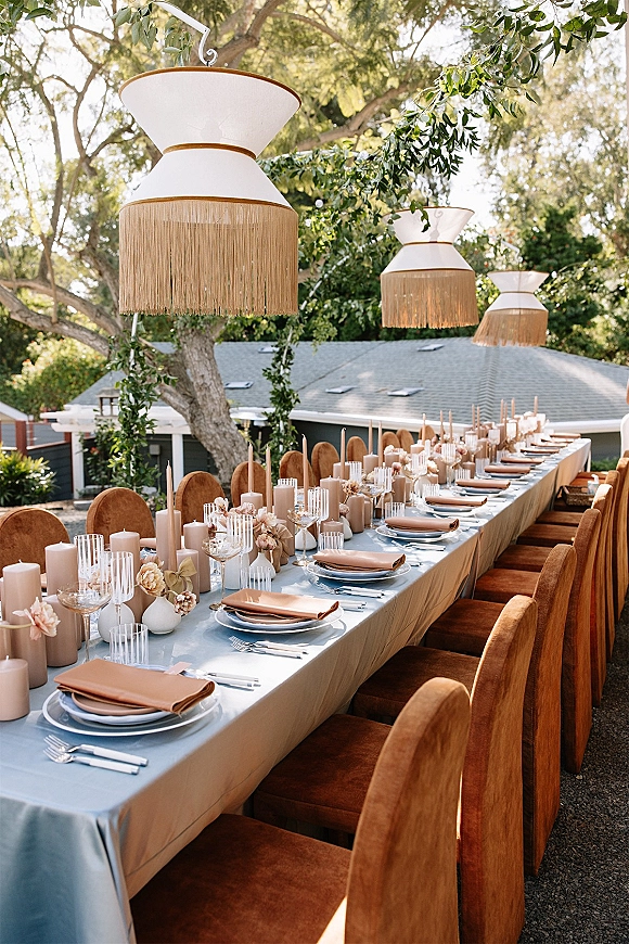 Reception tablescape with a long banquet table wedding setup, taper and pillar candles, bud vases, and greenery garland in a courtyard
