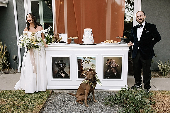 Wedding dessert table with a simple white cake and dessert platters on an outdoor patio, framed dog portraits beside bride and groom with dog