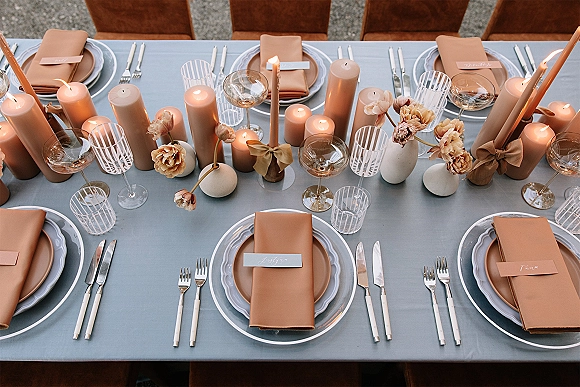 Reception tablescape wedding table setting with linen cloth, tan napkins, glass chargers, striped tumblers, and mixed taper and pillar candles on gravel