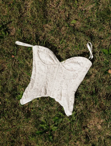 Wedding corset with lace bustier cups and satin ribbon straps laid on a grass lawn, highlighting the structured bridal corset top