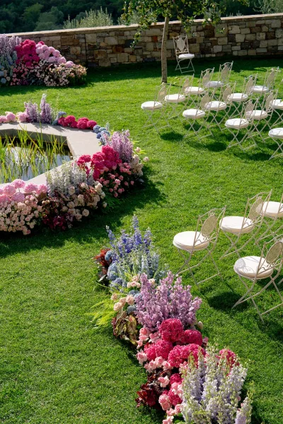 Ceremony aisle decor with outdoor ceremony aisle flowers, pastel hydrangea and rose clusters lining white chairs on a green lawn near a pond