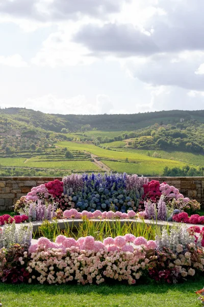 Ceremony backdrop with hydrangea wedding flower wall accents in pink, purple, and blue, framed by greenery on a stone wall terrace vista