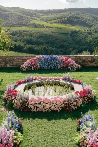 Ceremony floral decor with pastel hydrangeas and roses arranged in a circular wedding ceremony setup on green lawn by a garden pond