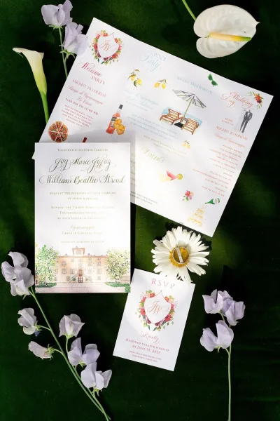 Wedding invitation suite flat lay with invitation, RSVP and illustrated cards, calla lily and sweet peas on a dark green surface