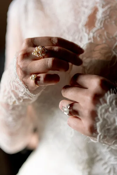 Wedding rings with diamond engagement ring and pearl ring resting on lace bridal sleeves against a soft fabric backdrop in warm light