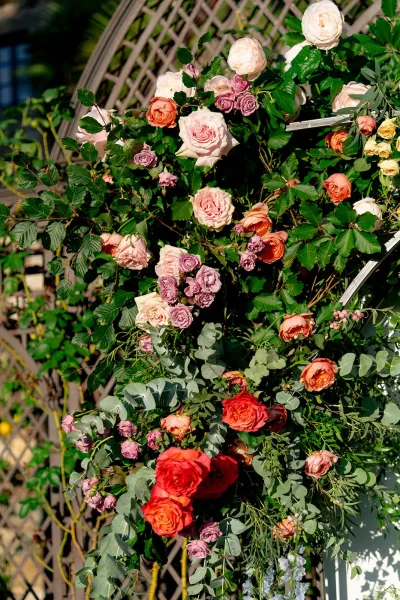 Wedding floral arch with garden rose clusters and greenery on a lattice trellis, glowing in sunlight amid outdoor garden foliage