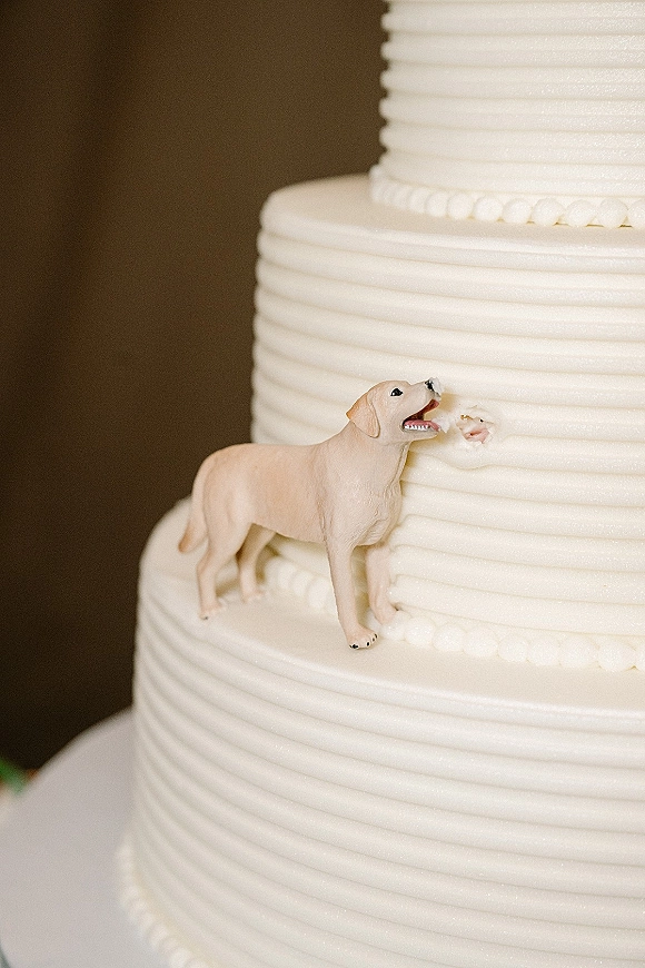 Wedding cake topper with dog cake topper figurine on a white tiered cake with ridged buttercream frosting against a brown wall backdrop