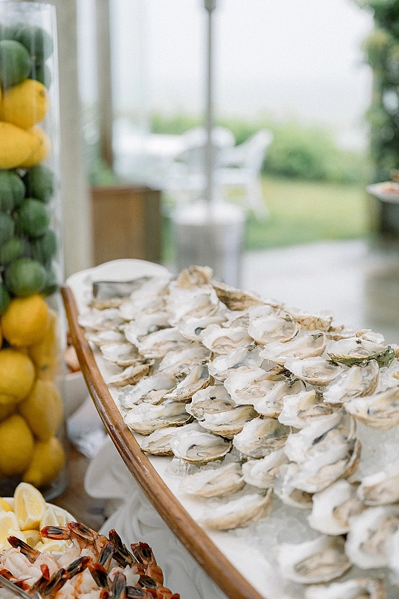 Oyster bar with oysters on ice and shrimp cocktail on a wooden tray, garnished with lemon slices, set on an outdoor lawn patio