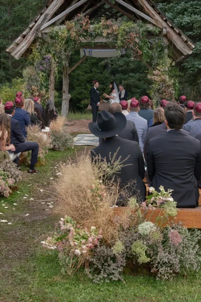 Ceremony moment at an outdoor wedding ceremony with couple under a rustic wood arbor, veil flowing, guests in yarmulkes by a white runner