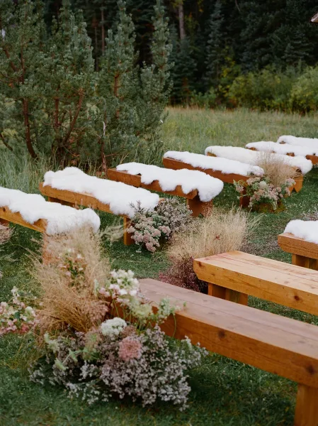 Ceremony seating with wood benches draped in white faux fur throws, lined by meadow flowers and dried grasses in a forest meadow setting