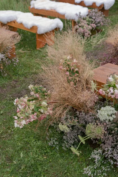 Ceremony aisle decor with outdoor ceremony aisle flowers in low hydrangea and dried grass clusters beside wooden benches on a lawn