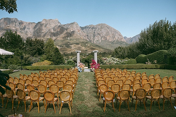 Outdoor ceremony setup with garden wedding ceremony chair rows, aisle runner and floral arrangements facing altar columns and mountain range backdrop