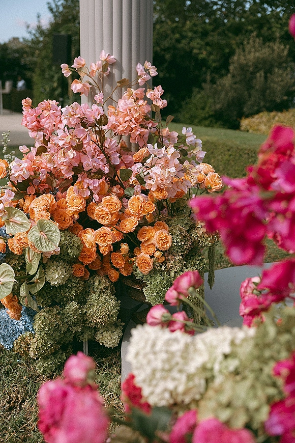 Wedding floral arrangement of roses, sweet peas, and hydrangeas with anthurium greenery at a white column in a garden walkway
