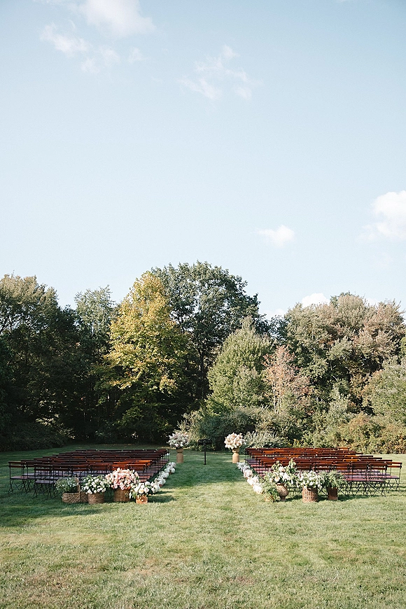 Outdoor ceremony setup with garden wedding ceremony seating, wooden chairs lining a symmetrical aisle with floral baskets on a green lawn