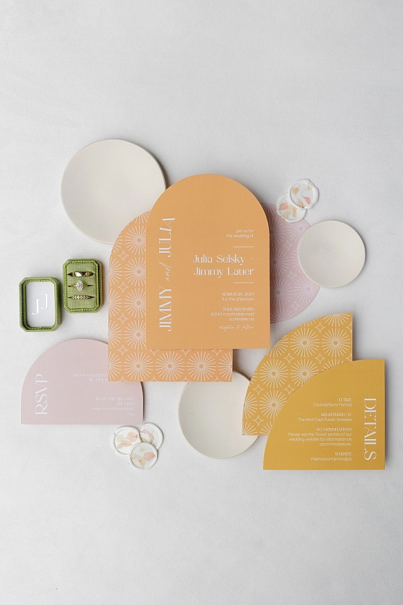 Invitation suite with arch wedding invitations, RSVP and details cards, patterned envelopes, wax seals, and rings on a white backdrop