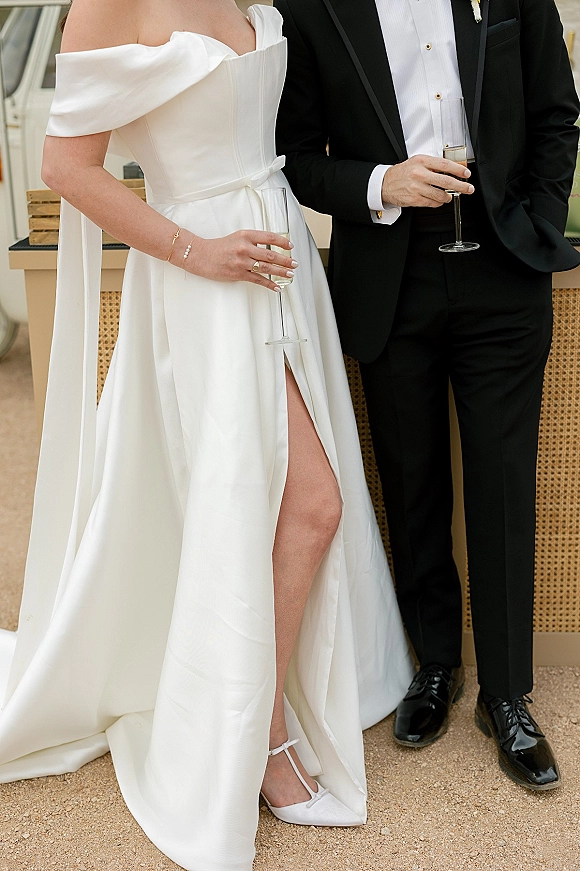 Wedding couple portrait with bride and groom champagne toast, her off-shoulder slit gown and his black tux, at an outdoor bar counter