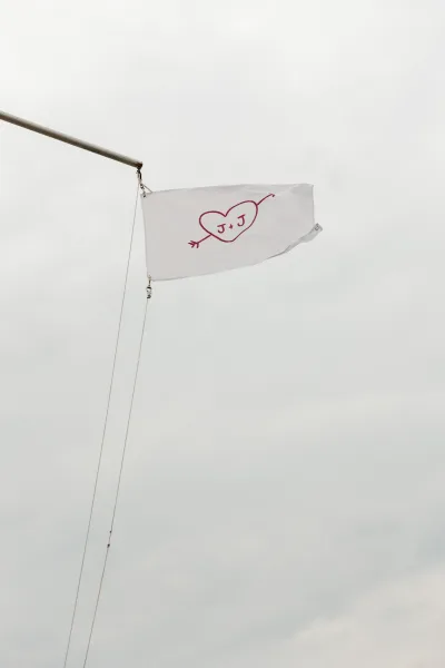 Wedding flag with a custom couple monogram and red heart motif flutters against an overcast sky, a clean, minimal wedding detail.