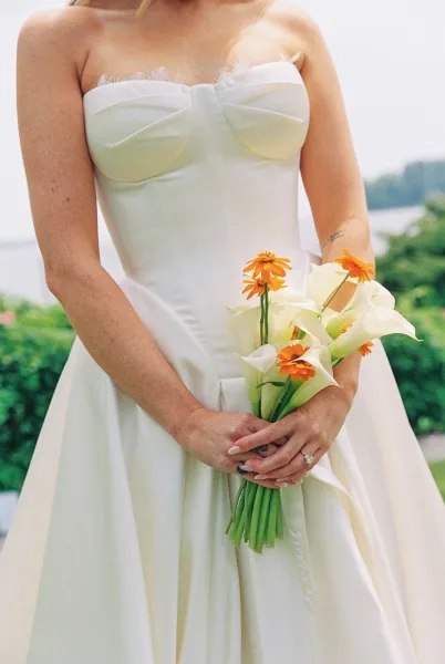 Bridal bouquet of white calla lilies, a slim calla lily bouquet held by the bride near garden greenery and water, diamond ring glinting.
