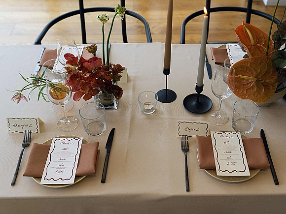 Reception tablescape with modern wedding tablescape style, beige tablecloth, black candle holders, taper candles, orchids, and anthurium centerpieces