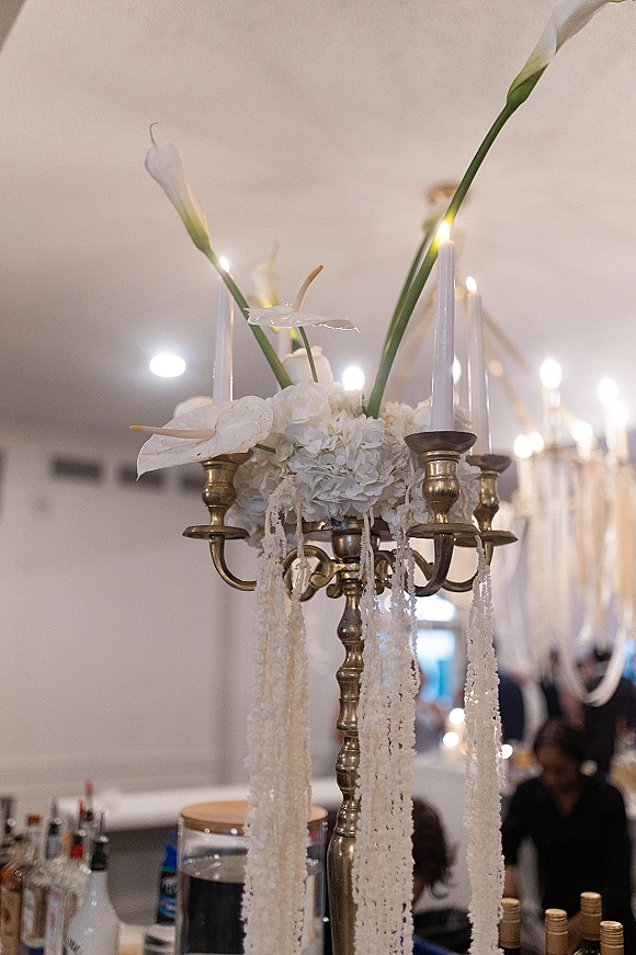 Wedding centerpiece with a brass candelabra and taper candles surrounded by white calla lilies under hanging garlands in a reception room