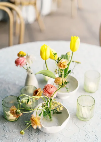 Wedding tablescape with spring wedding centerpieces in clustered bud vases of tulips and ranunculus, ribbed glass votives on textured linen