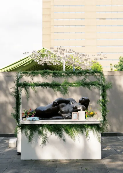 Wedding welcome table with framed photos, candles, and greenery garland on a sunlit outdoor terrace beneath a tent canopy