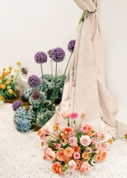 Wedding ceremony florals with ceremony aisle flowers in peach, pink, and blue on moss, set against a minimal white wall and terrazzo floor